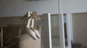 White women's shoes with a pointed toe. Beige Heeled sandals hang from glass railings. Classic women's shoes. Stylish accessory. wedding details. Bride morning. Business lady. Fees at the hotel.