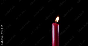 A single red candle burning. Isolated candle burning with dark background. Red paraffin candle with yellow shades burns on a black background. Background or illustration of remembrance or celebration.