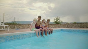 Smiling kids sit on poolside with feet in water - Free Stock Video