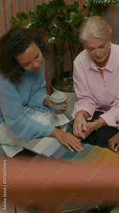 Vertical high angle slowmo shot of female clothing designer with diverse team of assistants examining textile color palette on table while developing new collection in modern office
