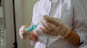 A female nurse prepares an injection syringe, fills a syringe from an ampoule with liquid, provides first aid. Woman's hands in rubber white gloves are injecting into a syringe.