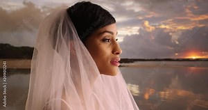 Side view of gorgeous bride on the beach, joyful and excited, Black woman in cute elegant dress with veil getting married, sunset outside, 4k