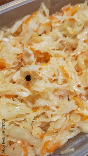 Sauerkraut with shredded carrots and black peppercorns in a clear container. Extreme close-up shot focuses on the glistening texture of the fermented vegetables.