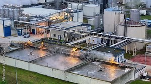 Industrial plant with smoking stacks, the scene lit by stark yellow lights, suggesting a significant ecological impact.