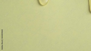 Liquid drops of yellow paint cosmetics product flowing on the yellow surface. Macro shot of pastel yellow shower gel dripping on the wall
