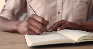 clip-1065238201-african-woman-sitting-desk-holding-pen-making