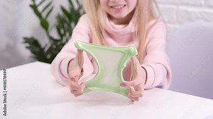 Hands with green slime close up. Girl stretching slime to the sides. kids hands playing slime toy. Making slime on white. Trendy liquid toy sticks to hands and fingers Slow motion.