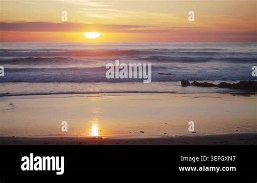 Cinematic 4K slow motion footage (150 fps) of gentle ocean waves rolling onto the beach during a majestic golden sunset. The warm evening light illuminates the water and sky, Guincho beach, Portugal Stock Video Footage - Alamy