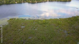 4k aerial clip flying from land over a canal and wetlands to the lake with blue water and green trees in sunny summer conditions, in mid michigan on Cranberry Lake, near Harrison MI.