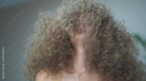 Slow motion. Close-up of a beautiful young woman with curly hair, smiling, looking at the camera, waving her hair in different directions. High quality FullHD footage