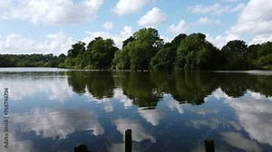 Scenic view of the reflections of clouds, sky, and trees in the waters of Mote Park Lake, located in Maidstone in the county of Kent in United Kingdom.
