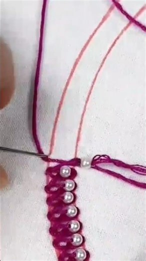 sewing many small white pearls precisely onto a white fabric using a needle and purple thread loop