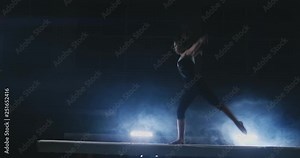 The girl performs a trick on a log in backlight and slow motion in sports gymnastic clothing. Smoke and blue. Jump and spin on the balance beam