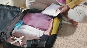 Making check list of things to pack for travel. Woman writing paper take note and packing suitcase to vacation writing paper list sitting on room, prepare clothes into luggage, Travel vacation travel