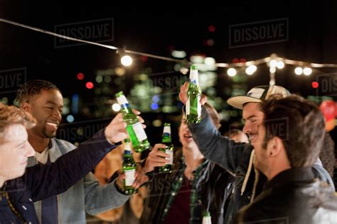 Young Men Drinking Beer And Dancing At Rooftop Party Stock Photo