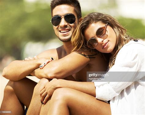 Happy Young Couple Sitting On The Beach Enjoying Warm Sun High Res