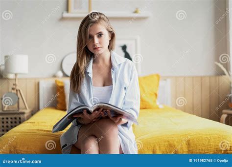Encantadora Mujer Leyendo Una Revista Sentada En La Cama Del Dormitorio Imagen De Archivo