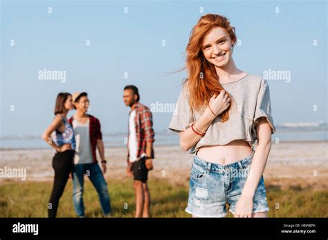 Happy Redhead Young Woman Standing While Her Friends Talking Outdoors