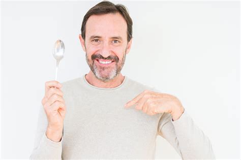 Senior Man Holding Silver Spoon Over Isolated Background With Surprise