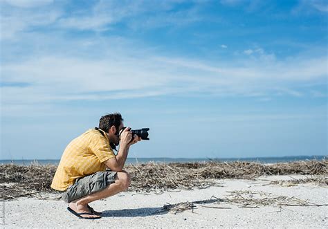 Man On A Beach Takes A Photo With A Digital SLR Camera By Stocksy Contributor Cara Dolan
