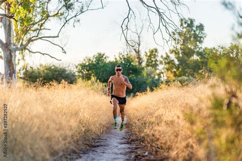 Full Body Shirtless Male Athlete With Sunglasses Running On Narrow Footpath Among Tall Grass