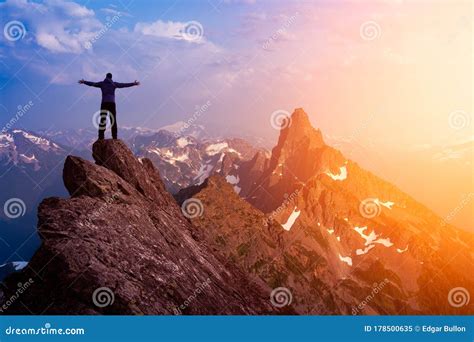 Adventurous Man Hiker With Hands Up On Top Of A Steep Rocky Cliff