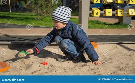 Little Boy Playing In Sandpit On Palyground And Building Sand Castle