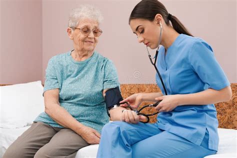 Nurse Measuring Senior Woman`s Blood Pressure In Hospital Ward Stock