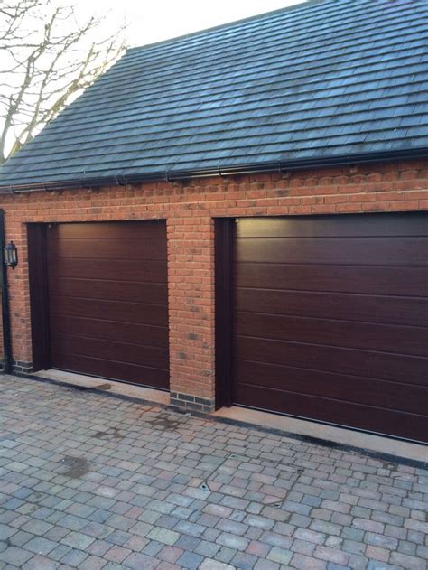 Two Brown Garage Doors In Front Of A Brick Building On A Cobblestone