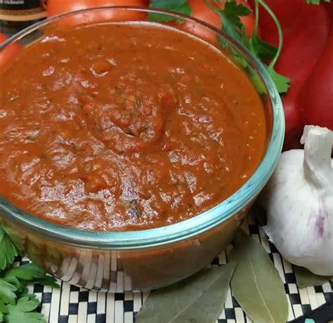 A glass bowl filled with red sauce next to some vegetables and garlic