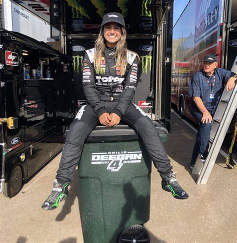 A Woman Sitting On Top Of A Green Trash Can In Front Of A Large Truck