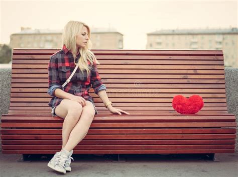 Sad Lonely Girl Sitting On A Bench Near To A Big Red Heart Stock Photo