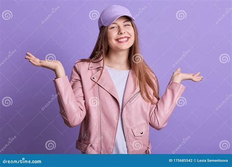 Portrait Of Young Woman Wearing Pink Leather Jacket Looking Camera Spreading Hands Aside Happy