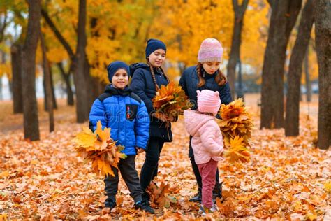 Children Playing With Yellow Maple Leaves In Autumn City Park Fall