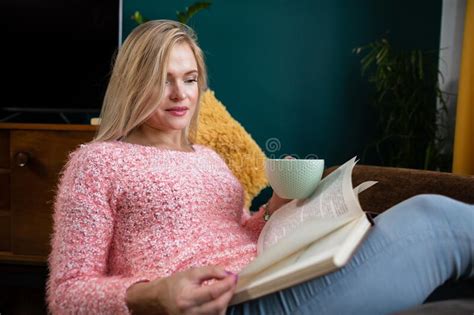 a girl reads a book with a cup in her hand while resting stock image image of jeans