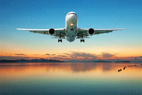 Airplane Flying Over Sea Against Sky At Sunset Stock Photo
