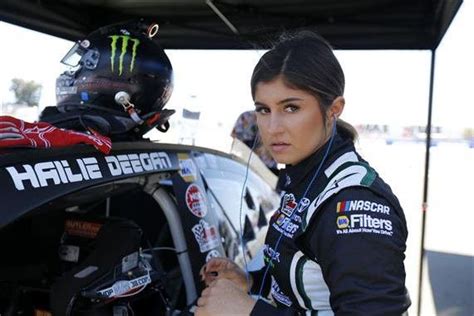 A Woman With A Helmet On Standing Next To A Race Car In A Pit Area