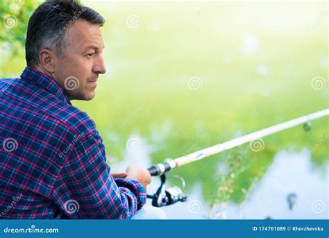 Mature Man Sitting On The River Bank And Fishing Summer Outdoor