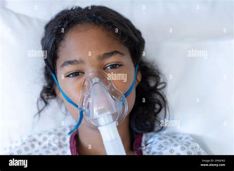 Portrait Of Sick Mixed Race Girl Lying In Hospital Bed Wearing Oxygen Mask Ventilator Stock