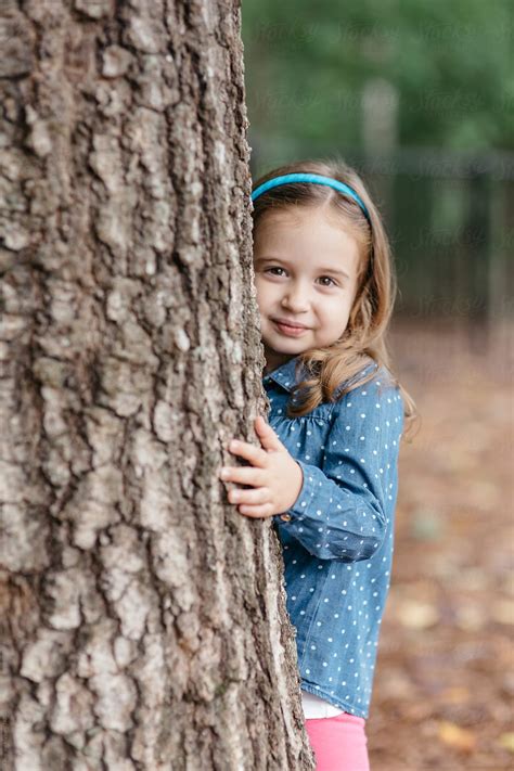 Beautiful Young Girl Peeking Out From Behind A Tree Del Colaborador