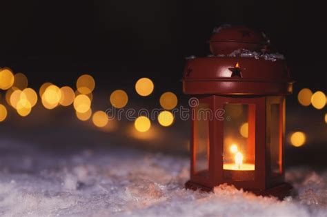 Lantern With Burning Candle And Christmas Lights On Snow Outdoors
