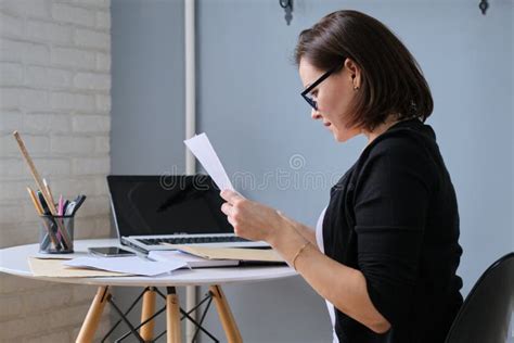 Mature Business Woman Sitting At Desk In Office Reading Paper Document