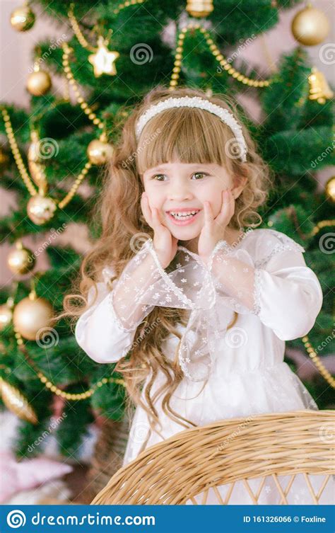 Cute Girl With Long Hair In A White Ball Gown By The Christmas Tree In