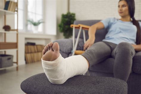 Patient With Broken Leg In Plaster Cast Sitting On Sofa At Home With