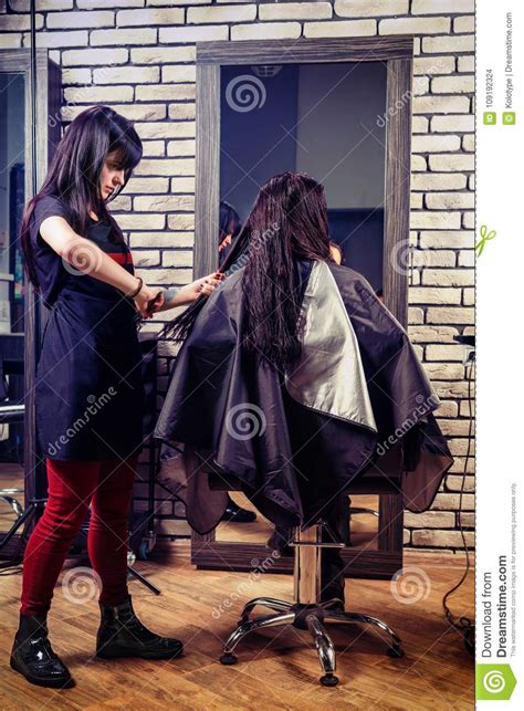 Professional Hairdresser Combing Hair Of Young Brunette Woman While She