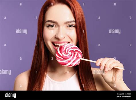 Woman With Red Dyed Hair Biting Lollipop On Purple Background Stock