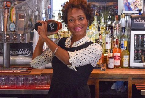 A Woman Holding Up A Bottle In Front Of A Bar With Liquor Bottles On It