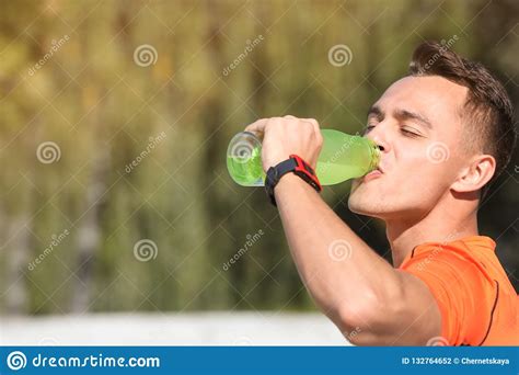Young Sporty Man Drinking Water From Bottle Outdoors On Sunny Day