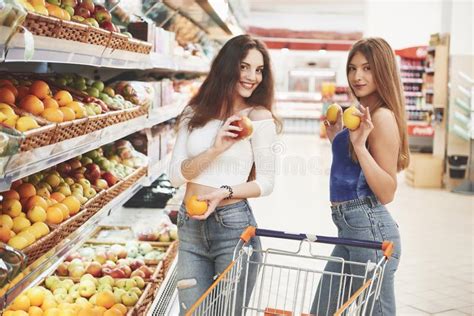 Two Women Choose Seasonal Fruits In The Supermarket Grocery Store Stock