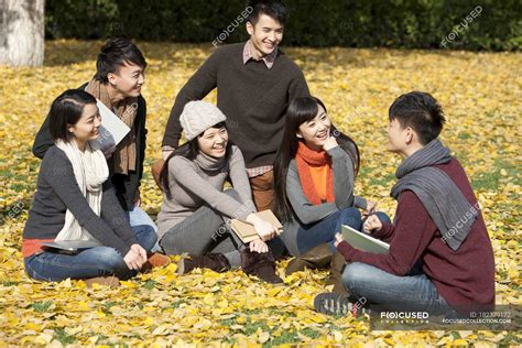Chinese College Students Sitting With Books And Talking In Autumnal